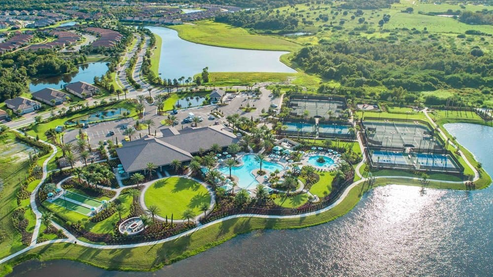 Aerial view of a resort-style community with pools, tennis courts, landscaped lawns, and surrounding lakes and greenery—perfect for enjoying RealFood-inspired outdoor gatherings.